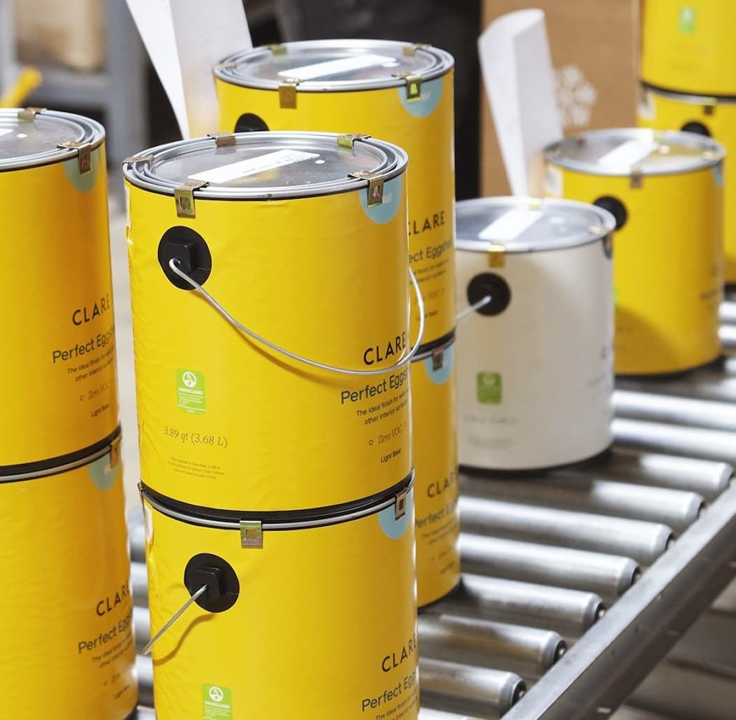 Yellow Clare paint cans moving along a warehouse conveyor