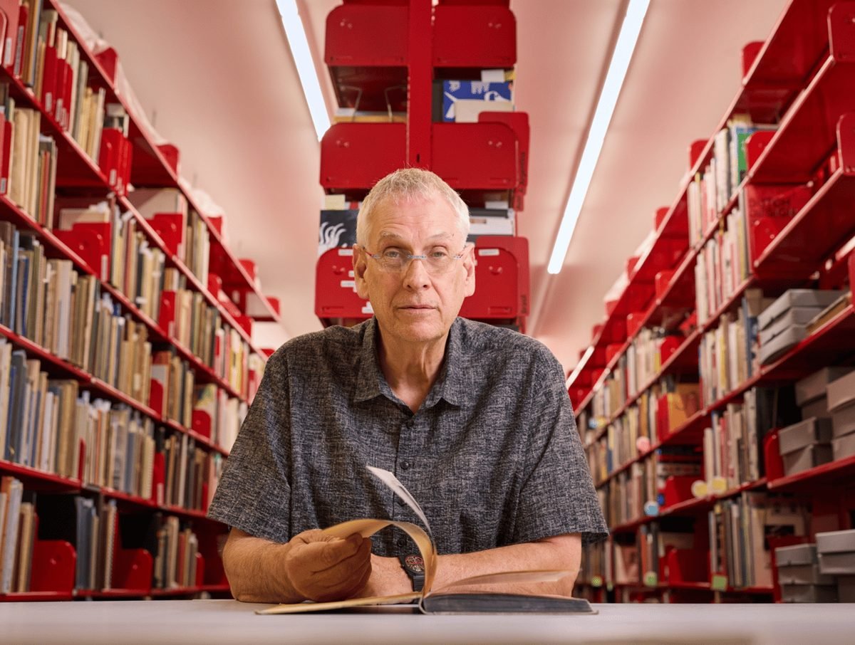 Rob Saunders at a table between the red shelves of Letterform Archive