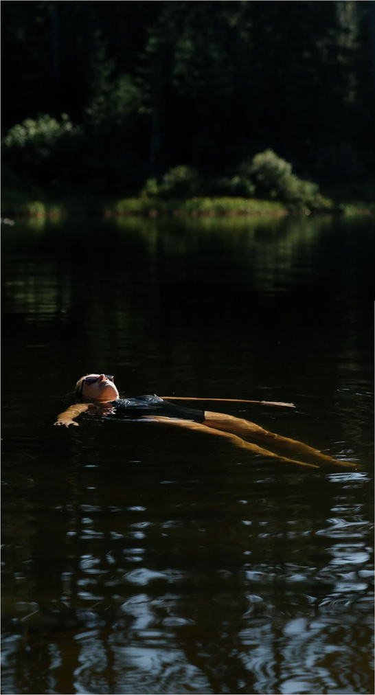 A woman floating on her back in the still water of a forest lake
