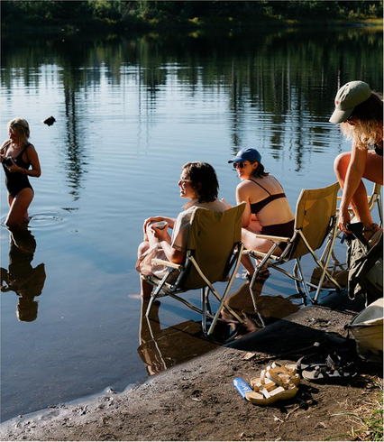 Friends in camp chairs on the lake shore while one of them wades into the water