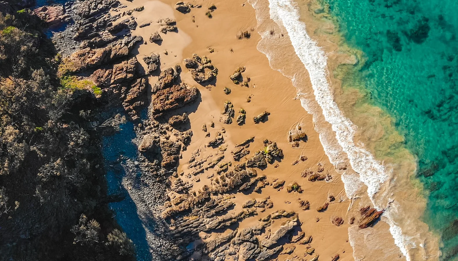 Aerial view of a rocky coastline with turquoise water and a strip of golden sand
