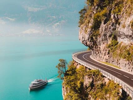 Coast road cut into cliffs above blue water with a cruise ship below
