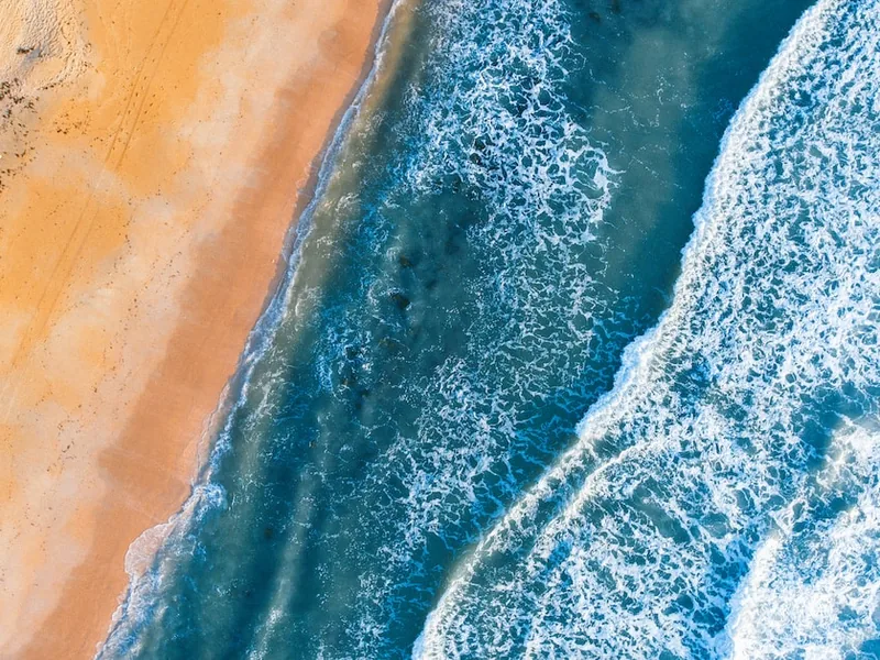 Aerial view of white surf meeting an orange-sand beach