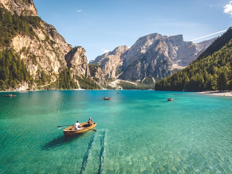 Rowing boat crossing the turquoise water of Lago di Braies below limestone peaks