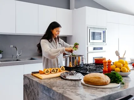 Woman cooking at a marble kitchen island with vegetables and a loaf of bread