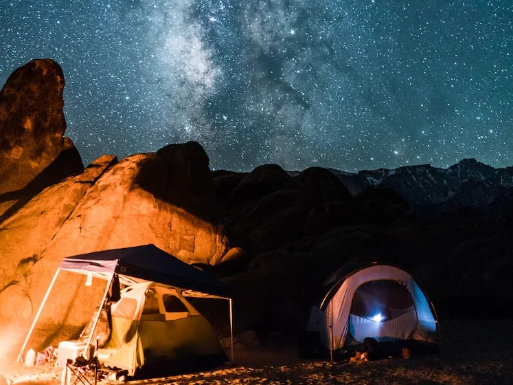 Milky Way over a lit tent and a lantern at a desert camp