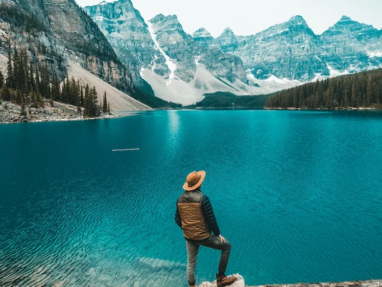 Hiker standing on a boulder above the turquoise water of Moraine Lake