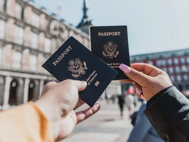 Two hands holding up passports in a sunlit city square