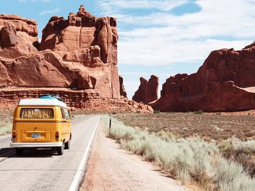 Yellow Volkswagen camper van driving a desert road past red sandstone towers
