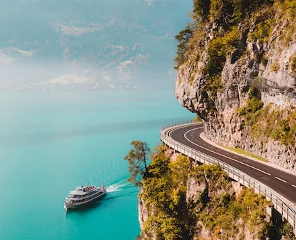 Coast road cut into cliffs above blue water with a cruise ship below