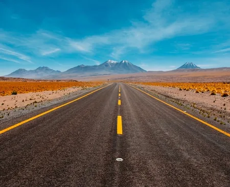 Straight road across the Atacama desert towards distant volcanoes