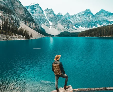 Hiker standing on a boulder above the turquoise water of Moraine Lake