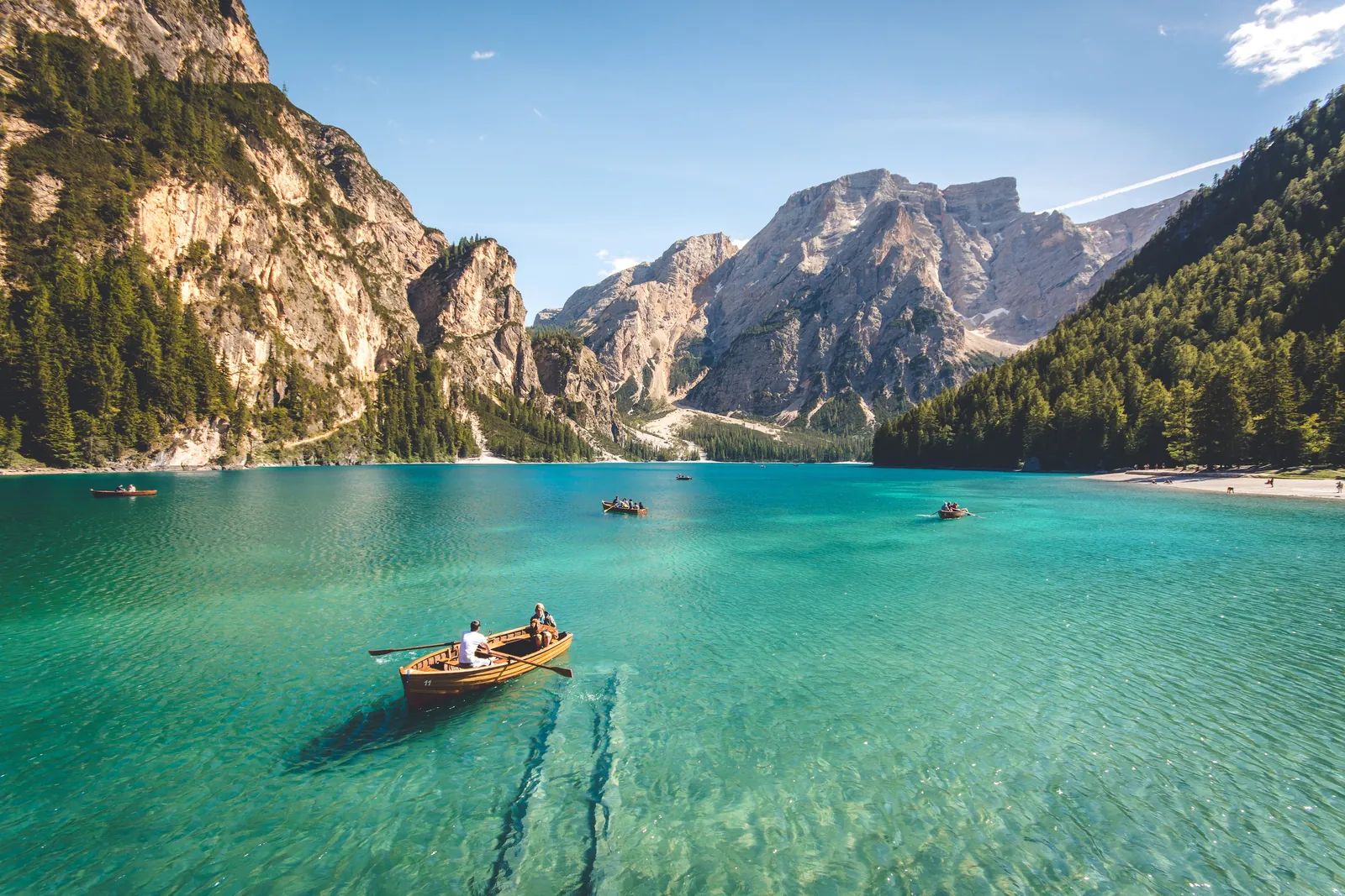 Wooden rowing boat on the green water of Lago di Braies, forested slopes and grey peaks behind
