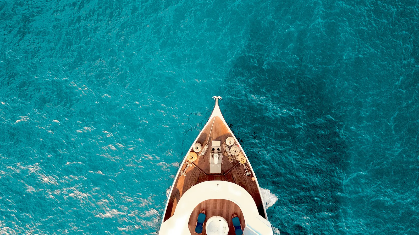 Bow of a white sailing boat over clear turquoise water, seen from above