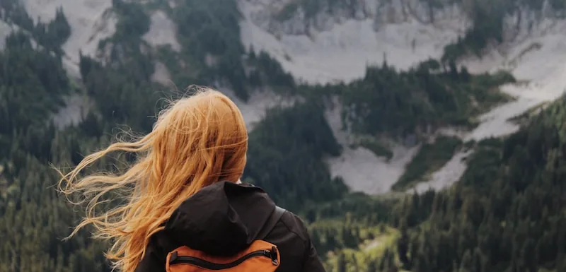 Woman with a backpack looking out at an alpine ridge, hair blown by the wind