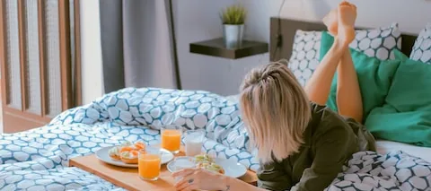 Woman lying on a bed with a breakfast tray of juice and pastries