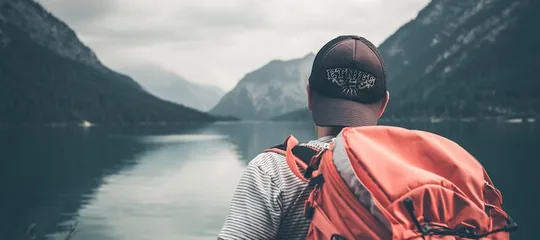 Hiker with a red backpack looking across a lake to mountains