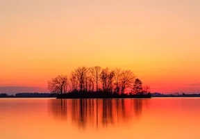 Silhouetted island at sunset, red sky mirrored in still water