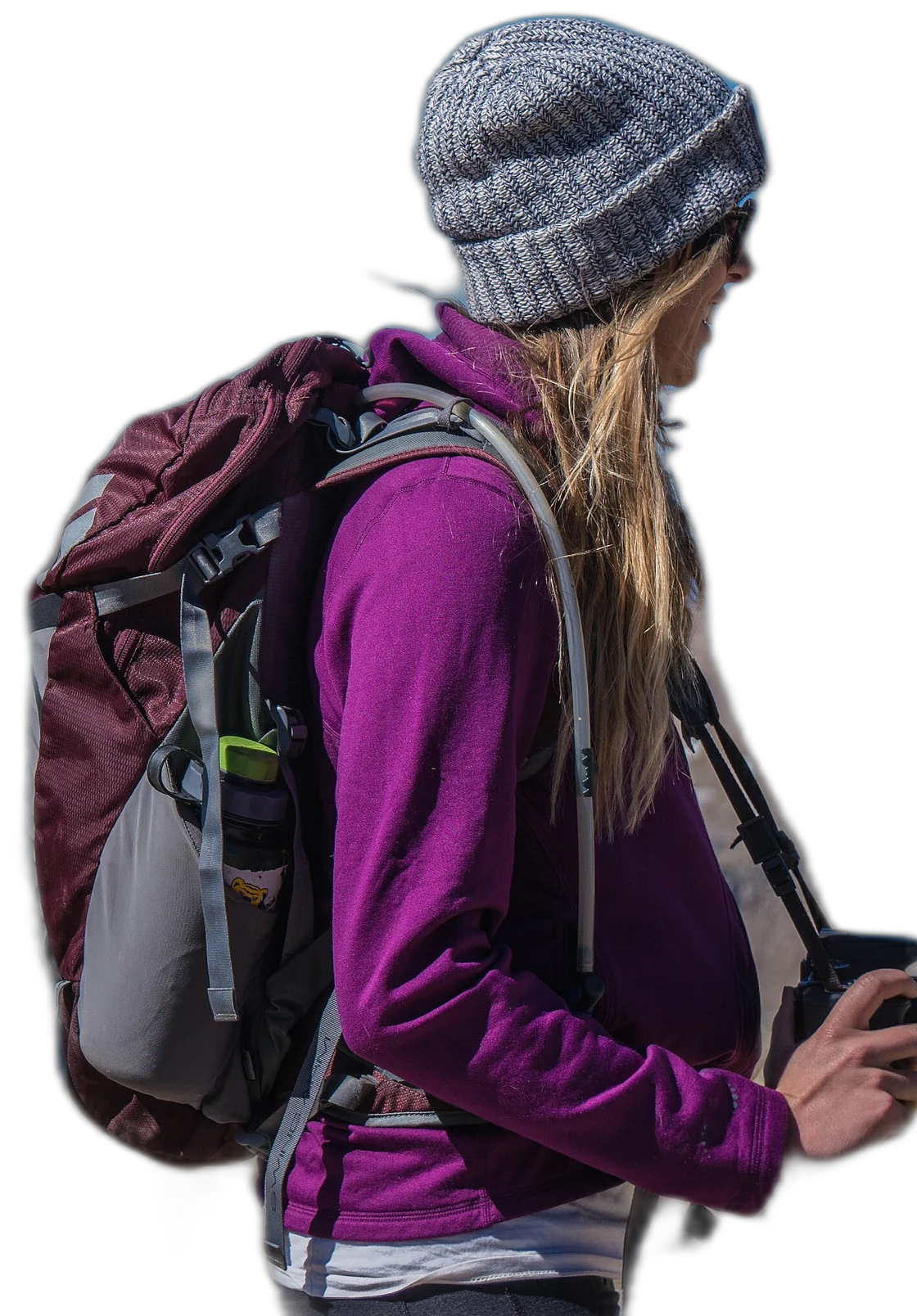 Woman in a beanie with a hiking backpack holding a camera outdoors
