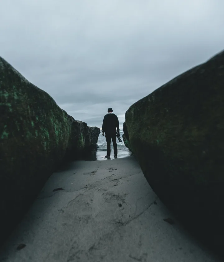 Lone figure on a misty road between dark cliffs